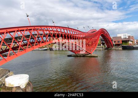 Amsterdam, The Netherlands-May 2021: Low angle side view of the red metal snake like Pythonbrug with wooden steps which is a footbridge crossing over Stock Photo