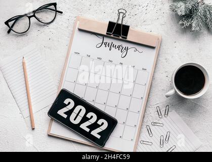 January calendar flat lay. Top view of January calendar on table and year 2022 on display of mobile phone. Stock Photo
