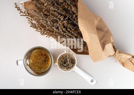 Glass of herb tea, tea strainer and Wormwood twigs wrapped in brown paper. Stock Photo