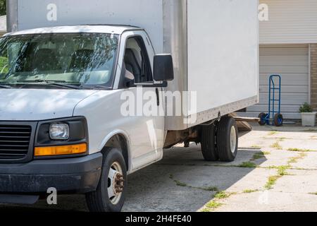 moving van waits in the driveway with a blue dolly ready to load up for a home move Stock Photo