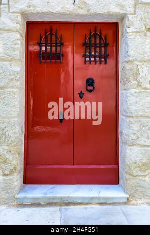 Red wooden door with black forged vintage lion head shaped ring knocker and gratings on small windows Stock Photo