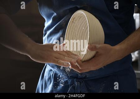 Male baker lightly flouring proofing basket for home made sourdough bread. Stock Photo