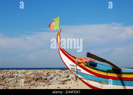 Ein buntes, altes Fischerboot aus Holz und mit rot grüner Flagge am Strand von Espinho, Portugal. Im Hintergrund Möwen und Meer. Stock Photo