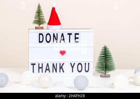 Christmas donation, charity. Donate and Thank you message on lightbox. Christmas decoration and garland on white desk. Front view, close up Stock Photo