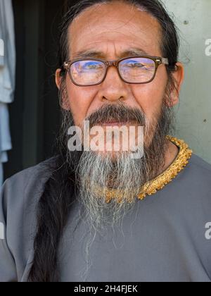 Pueblo, Peru - Mar 2018: Portrait of a preacher with a short gray beard, mustache i long black hair in glasses and in a grey cassock, on ship sailing Stock Photo