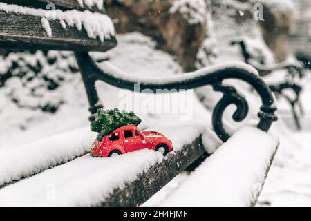 Close up selective focus photo of red Christmas toy car on snow covered park bench. Stock Photo