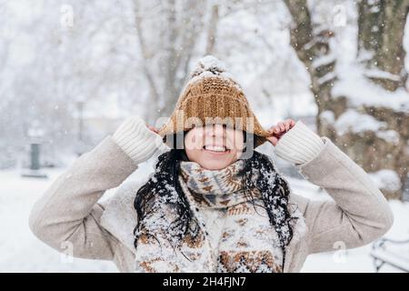 Portrait of beautiful young woman in winter clothes pulling her hat down over her eyes. Stock Photo