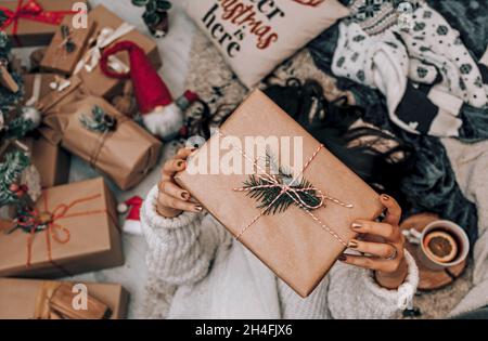 Top view of woman laying by christmas tree, holding wrapped christmas present. Stock Photo