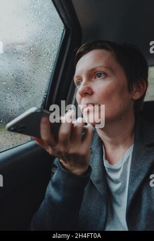 Serious businesswoman talking on mobile phone from the backseat of the car during the rain, selective focus Stock Photo
