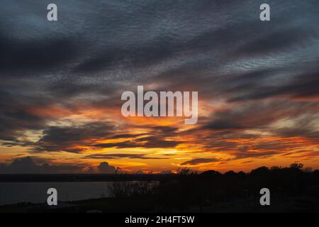 Low clouds forming a dramatic, fiery sky at sunset over water. Stock Photo