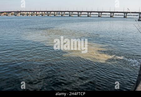 Dirty orange water from sewage pipeline mixes with river water. Clear border between two different water streams. Environmental pollution theme. Stock Photo