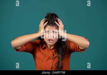 Frustrated young woman holding hands on head, madness concept, in studio on blue background Stock Photo