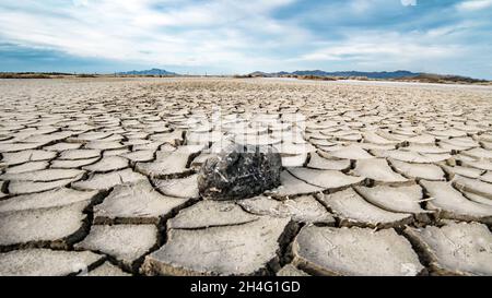 close-up of a dry soil with cracks due to drought caused by climate change, a mountain, dry grass and a sky with clouds. Stock Photo