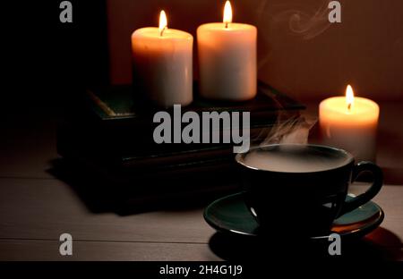 Cup of hot coffee with green  smoke, books and burning candles. Desk table in power supply cut Stock Photo