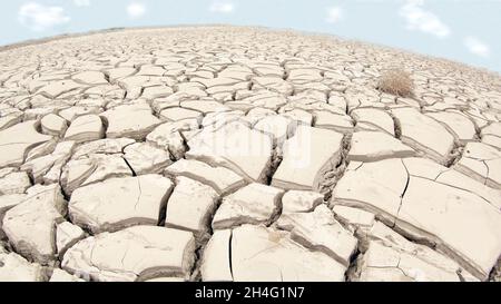 close-up of a dry soil with cracks due to drought caused by climate change, in the background a blue sky with few clouds. Stock Photo