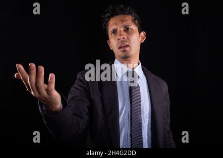 An angry businessman filing a complaint. Young adult can't believe his eyes and gets angry. Black man raises his hand in anger. Isolated on black Stock Photo
