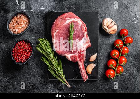 Cooking Raw Rib eye or Tomahawk beef steak with spices. Black background. Top view Stock Photo