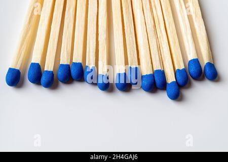 Bright blue wooden matches as a background with copy space. Row of matchsticks with blue heads over light gray surface. Several wooden matches. Stock Photo
