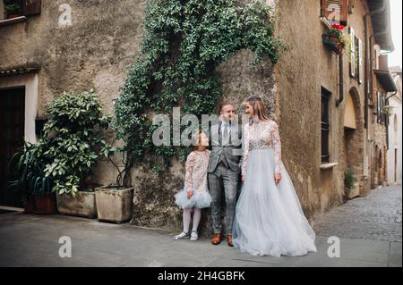 A happy young family walks through the old town of Sirmione in Italy.Stylish family in Italy on a walk. Stock Photo