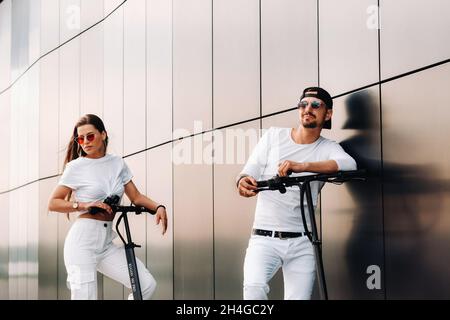 A girl and a guy are walking on electric scooters around the city, a couple in love on scooters Stock Photo