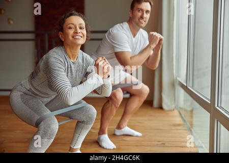 Smilng couple doing squats indoors during quarantine Stock Photo