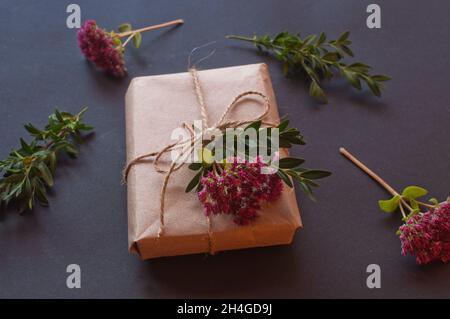 Craft gift box with knot natural with pink little flowers on black background. Sale concept on dark background Stock Photo