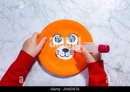 Step-by-step photo instruction on how to make a Tiger made of Paper Plate Tiger Craft with your own hands. The symbol of the new year 2022. STEP 4 . Glue eyes and nose Stock Photo