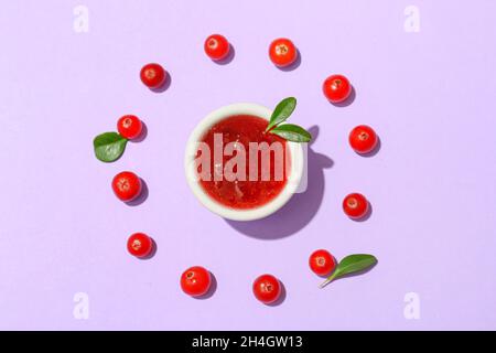Bowl of tasty lingonberry jam and berries on lilac background Stock Photo