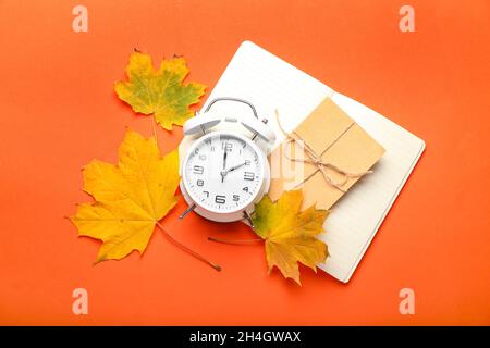 Alarm clock, notebook, envelope and autumn leaves on color background Stock Photo