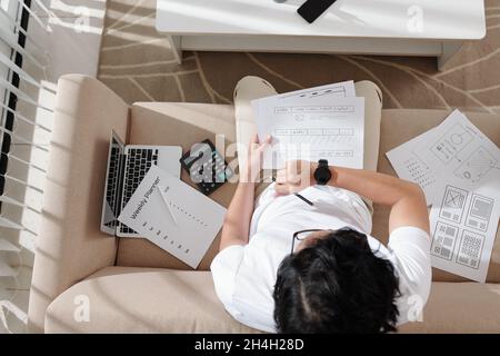 Freelance designer checking smartwatch when working with sketches at home and working on new project Stock Photo