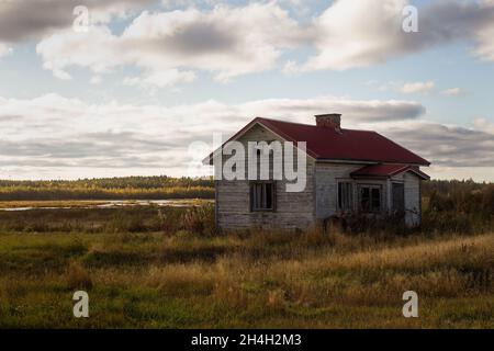 An old abandoned house by a small swamp lake. The windows of the house have been broken and the door hangs by the hinges. Stock Photo