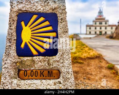 Kilometre zero with scallop shell, last kilometre stone of the Camino a Fisterra, in front of lighthouse, endpoint of the Way of St. James at Cape Stock Photo