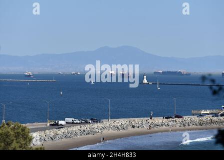 Sailboat passing the lighthouse at the Port of Los Angeles with container ships waiting at sea Stock Photo