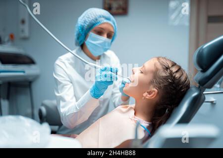 Side view of female dentist who treats teeth of little child patient in dental office. Dentistry  Stock Photo