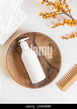 White plastic bottle with pump mock up, used for shampoo and conditioner for hair on wood tray and wood comb near on white background. Top view Stock Photo