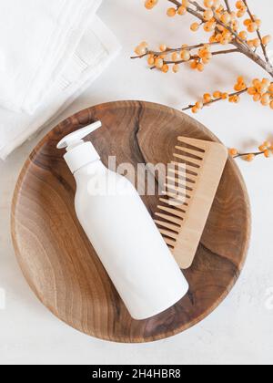 White plastic bottle with pump mock up, used for shampoo and conditioner for hair and wood comb near on wood tray on white background. Top view Stock Photo