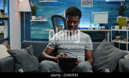 Young freelancer using digital tablet with touch screen for work online. Person with entrepreneur job holding gadget and working from home with modern technology. Man using internet Stock Photo