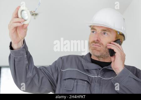 builder on the phone installing a spotlight in the room Stock Photo