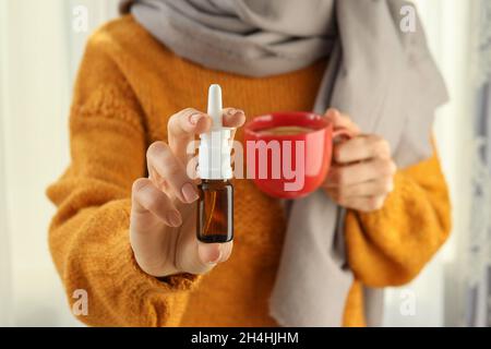 Woman holds nasal spray and cup of tea, close up and selective focus Stock Photo