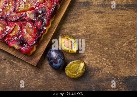Tart or pie with plums and plum halves on wooden rustic background. Top view, copy space Stock Photo