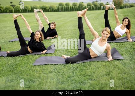 People practicing yoga on fitness mats on meadow Stock Photo