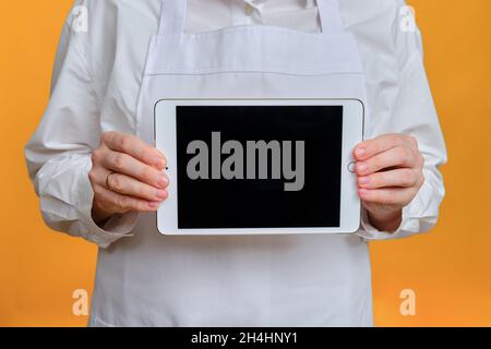 Man chef showing tablet ipad screen on yellow studio background, mockup copy space - Moscow, Russia, October 20, 2021 Stock Photo