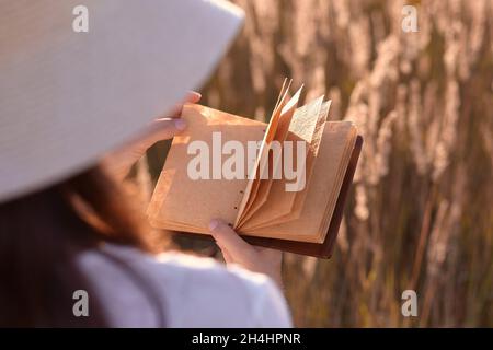 A woman holding an old notebook in her hand, a blank piece of paper. In the background there is a field meadow,.Copy space, close-up. Stock Photo