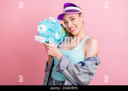 Photo of sweet young playful lady hold water gun wear jeans shirt cap isolated on pink color background Stock Photo