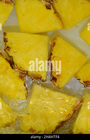Pineapple close-up in liquid with bubbles. Slices of ripe pineapple in water. Close-up fresh slices of yellow pineapple on white background. Vertical Stock Photo