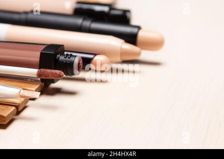 Make-up products to hide skin imperfections. Makeup concealers and foundation in a row on white wooden table. Side view, selective focus Stock Photo