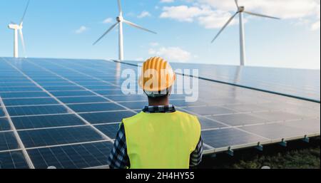 Engineer working for alternative energy farm - Wind turbine and solar panels - Focus on helmet Stock Photo