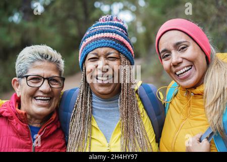 Portrait of multiracial senior friends having fun during trekking day in to the wood - Focus on right woman face Stock Photo