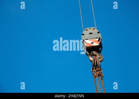 Hook bottle of a crane with ropes, eyelets, link chain and hook against a blue sky. The equipment is used for lifting heavy loads Stock Photo