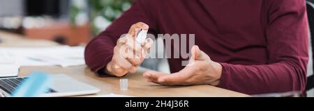 Cropped view of african american businessman using hand sanitizer near laptop in office, banner Stock Photo